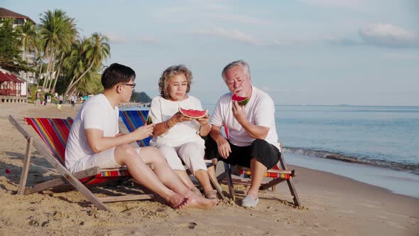 Couple of senior elderly retirement and a son enjoy and eating watermelon on the beach together