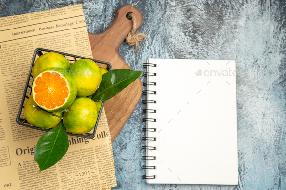 Above view of fresh citrus fruits newspaper on wooden cutting board and notebook on gray background
