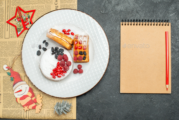 top view plate with berry tart and waffles paper xmas pendants a newspaper and a notebook on dark