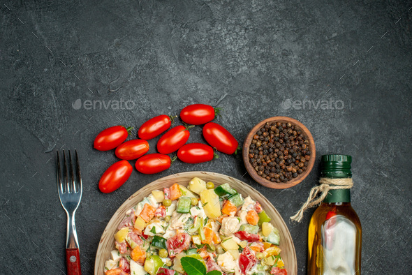 top close view of bowl of veggie salad with fork tomatoes pepper and oil on side and free place for