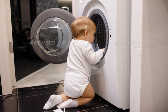Child climbing into front-loading washing machine. Side view. Lack of parental supervision