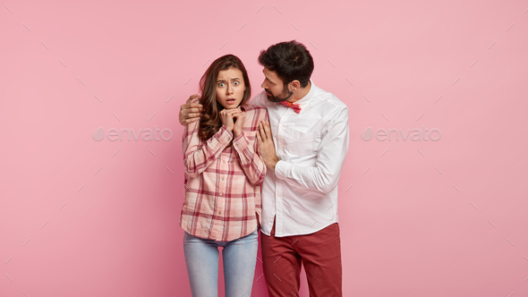 Stupefied female stares with bugged eyes, keeps hands together, her boyfriend embraces and asks not