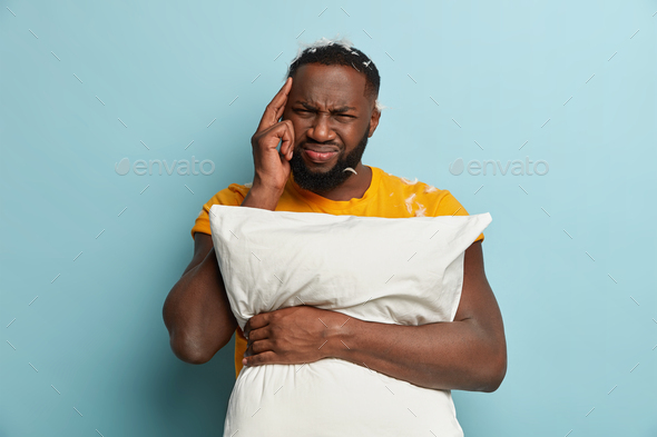 Stressful black man keeps finger on temple, suffers from headache after bad sleep because of noise,
