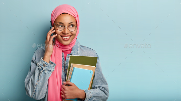 Happy delighted Islamic girl has phone conversation with friend, shares impressions after successful