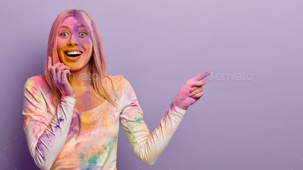 Shot of glad blonde woman splattered with multicolored powder, shows ...