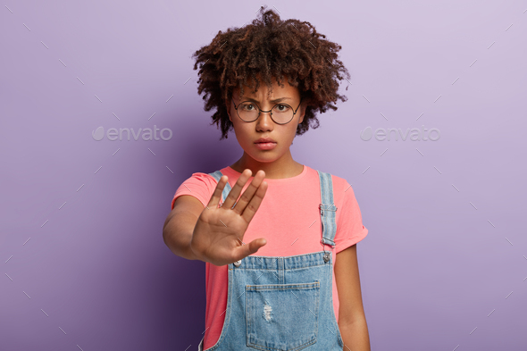 Photo of Afro American woman does stop gesture, has angry facial expression, demands stop talking, d