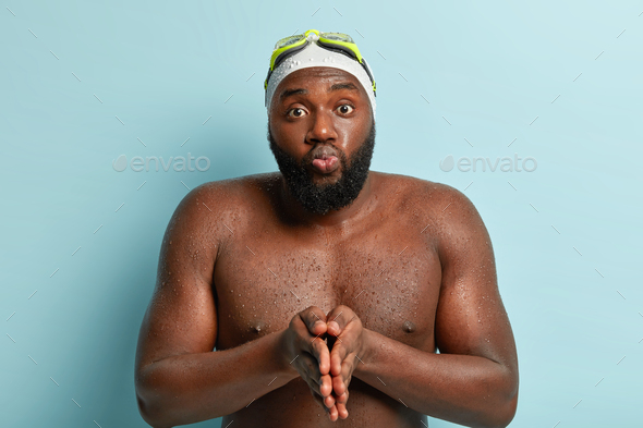 Active sportsman prepares for diving under water, keeps palms pressed together, folded lips, has bat