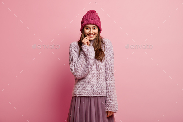 Pretty lady with satisfied expression, keeps hand near lips, hears something positive, wears winter