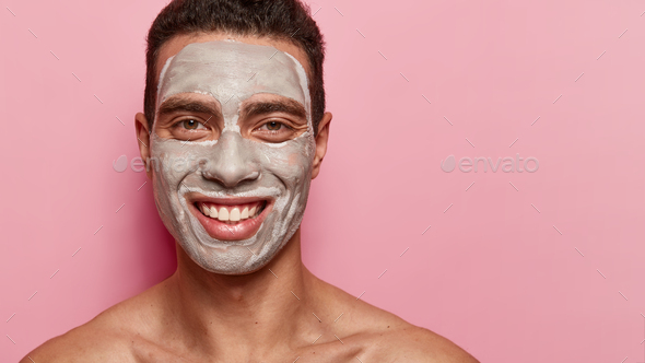 Positive young European man with satisfied expression, has clay mask, wants to have fresh healthy sk