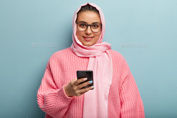 Photo of young beautiful woman with satisfied facial expression, checks email on cellular, enjoys on