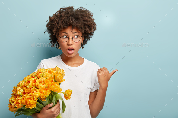 Surprised impressed woman with crisp hairstyle, holds bunch of yellow flowers, has bated breath, poi