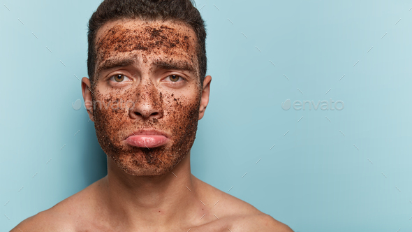 Photo of attractive man uses anti age coffee scrub, poses shirtless, purses lips, has spa treatments