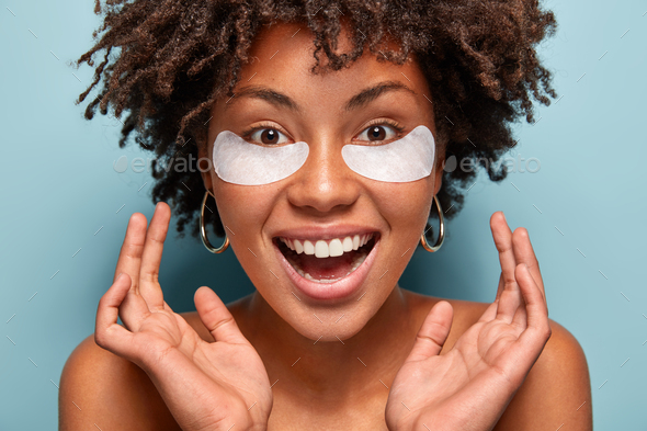 Headshot of ovejoyed beautiful woman reduces under eye puffiness, dark circles, applies moisturizing