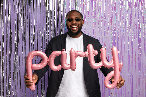 Joyful Afro American male student graduate has party with groupmates after leaving university, wears