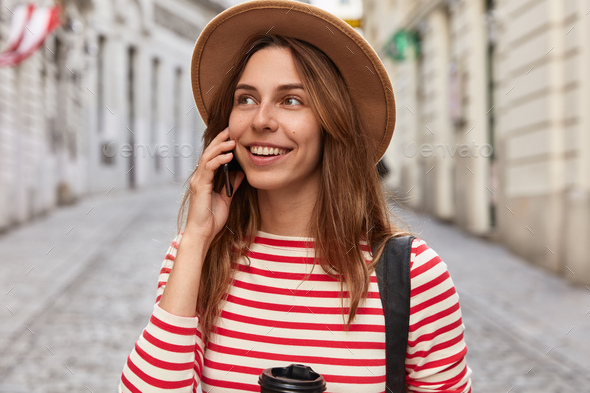 Outdoor shot of pleased Caucasian traveler talks on smart phone in roaming, enjoys cheap tariffs for - Stock Photo - Images