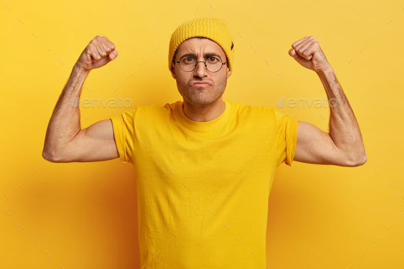 Photo of dissatisfied man with angry facial expression, raises hands, clenches fists, shows muscles,