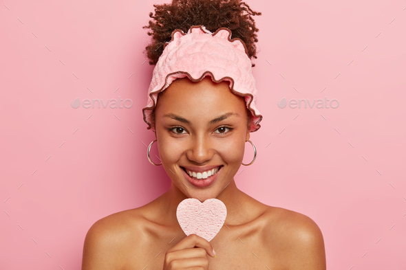 Pretty young Afro American lady with dark skin, holds cosmetic sponge for removing makeup, going to