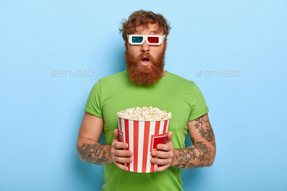 People and pastime concept. Scared bearded ginger man watches film which get his reaction, impressed