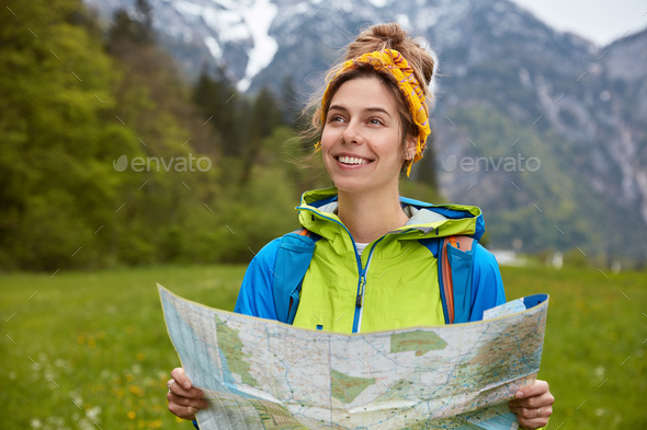 Satisfied female explorer has hitch hiking trip in mountains with snowy peaks, walks by foot on gree