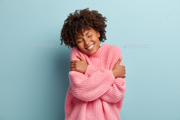 Love yourself concept. Photo of lovely smiling woman embraces herself, has high self esteem, closes