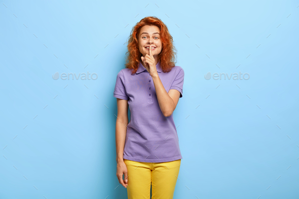 Studio shot of redhead beautiful woman has pleasant smile, tells secret to best friend about dating