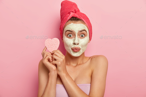 Portrait of young woman with mineral natural mask on face, has daily skin care treatment, holds cosm
