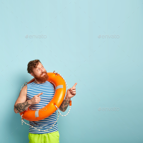 Man with red hair and beard points away, poses with rescue wheel, ready for rescuing drowning people