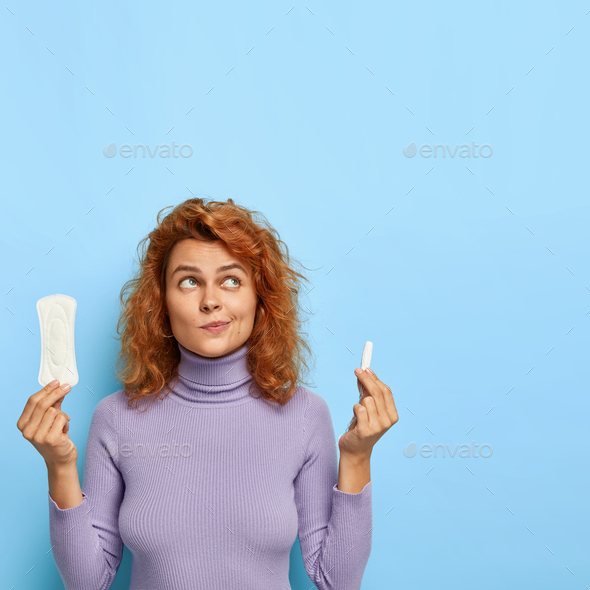 Hesitant woman thinks what better to choose during critical days, holds menstrual compress and tampo
