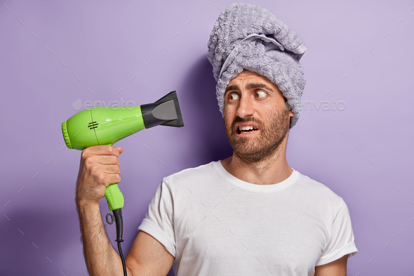 Something has gone wrong with my electric hair dryer. Frustrated man dries hair, wears towel on head