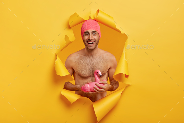 Summer vacation concept. Joyful man in good body shape, stands with bare torso, wears pink swimcap,