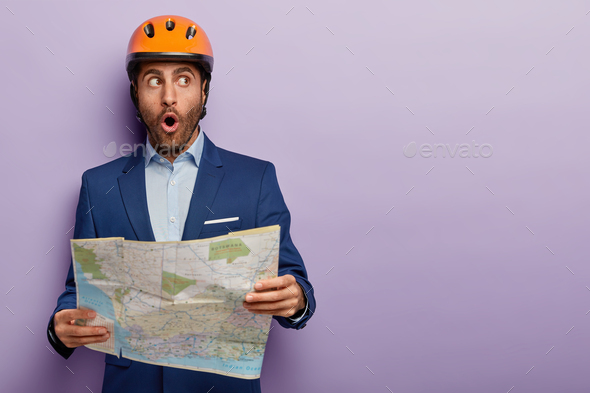 Elegant male builder tries find office, being on way to job interview, holds paper map, shocked choo