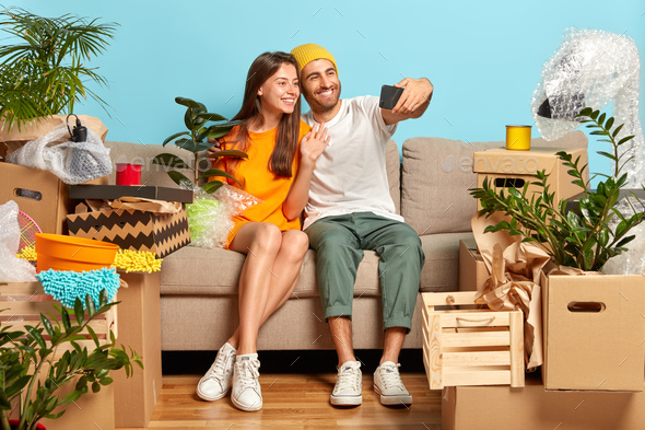 Relocating and changing house concept. Happy newlywed couple move to new abode, pose on cozy couch,