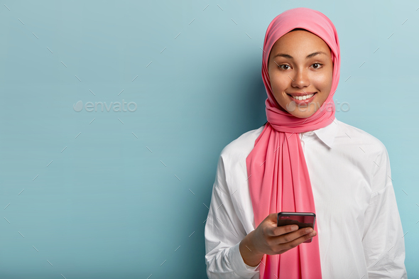Pleased Muslim woman uses cell phone to socialize, gives reply in online chat, posts something in so