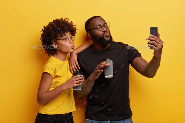 Funny surprised young woman makes grimace, poses for selfie, holds modern  smart phone, wears stylish spectacles, has long dark wavy hair, isolated  over yellow background, expresses wonderment Stock Photo | Adobe Stock