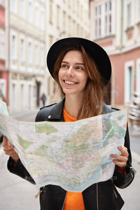 Happy holidaymaker searches right direction on map, explores new town with many sights, thinks about
