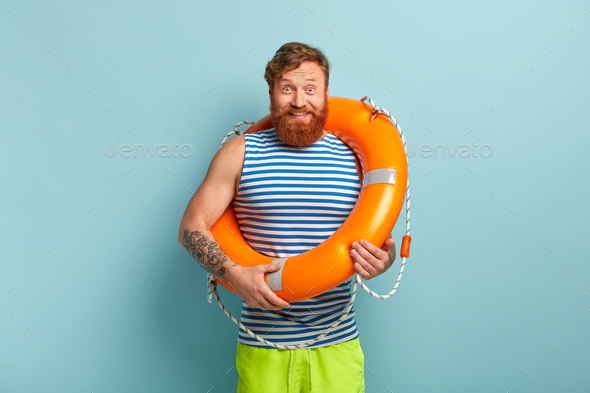 Happy carefree male with life preserver, has glad reaction, grins at camera, stands in casual clothe