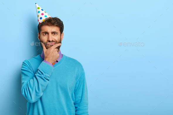 Thoughtful student thinks over graduation party, prepares for celebration, holds chin, looks serious