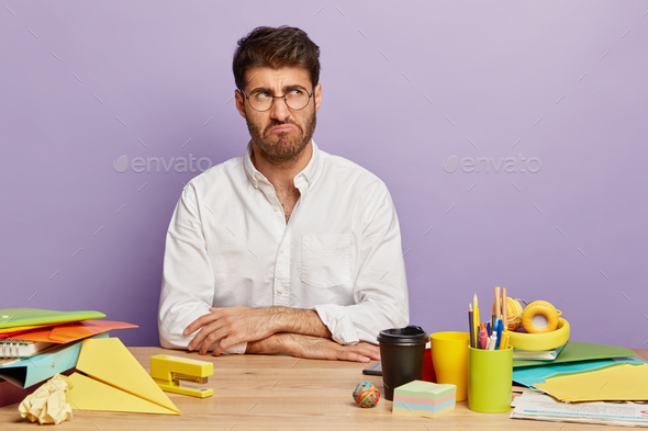 Horizontal shot of dissatisfied man smirks face, looks aside, dressed elegantly, wears spectacles fo