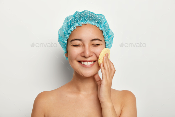 Beauty portrait of happy pleasant looking smiling lady uses cosmetic sponge for cleaning face, stand