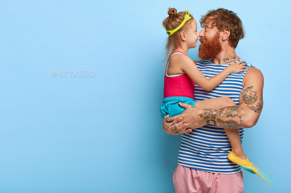 Lovely little child and her father touch noses, spend time together, girl wears goggles and fins, wa