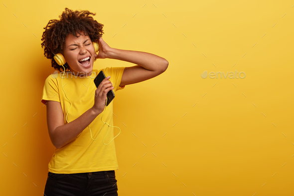 Pleased stylish dark skinned girl enjoys music from motivation playlist, enjoys free time for listen