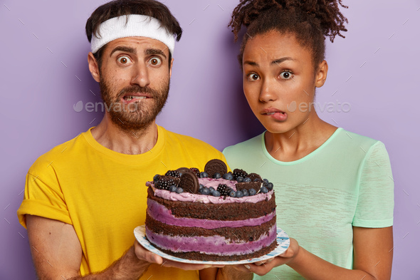 Cropped shot of young diverse couple bite lips, feel temptation after workout while look at deliciou
