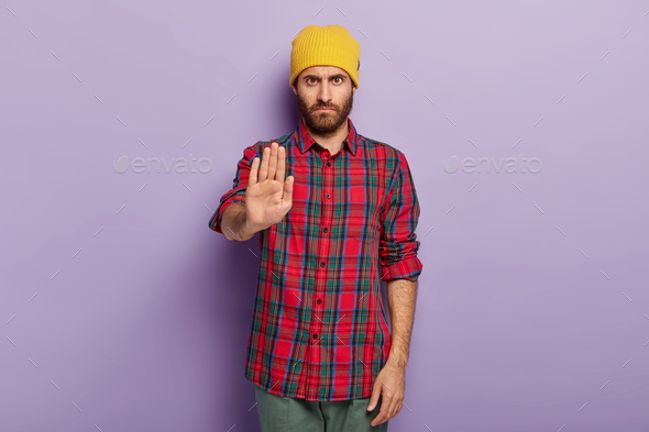 Photo of serious stern unshaven man shows stop gesture, dressed in fashionable clothes, refuses some
