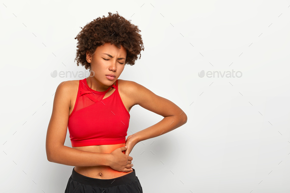 Dissatisfied African American woman holds aching hip, has kidney inflammation, touches location of p