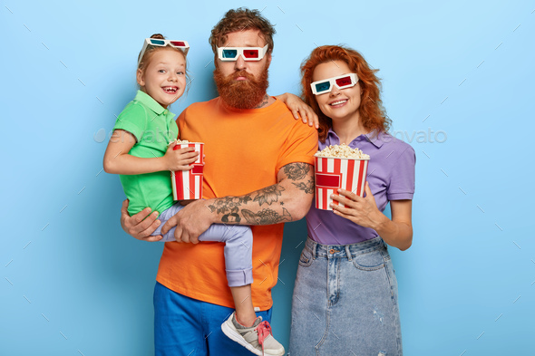 Horizontal shot of happy ginger family spend free time in cinema, come on premier of film, eat salty