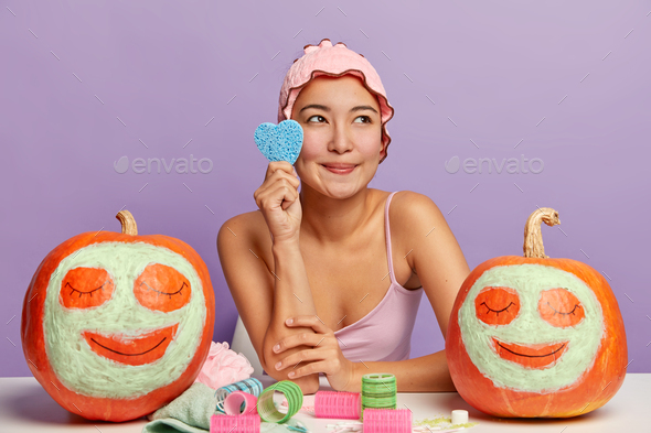 Photo of dreamy pleasant looking korean woman holds cosmetic sponge, cares about complexion, feels f