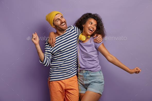 Friendly mixed race woman and man embrace and dance joyfully, spread hands, enjoy lovely music, feel