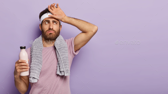 Exhausted athlete man feel thirsty and tired after hard cardio workout, wipes sweat on forehead, hol