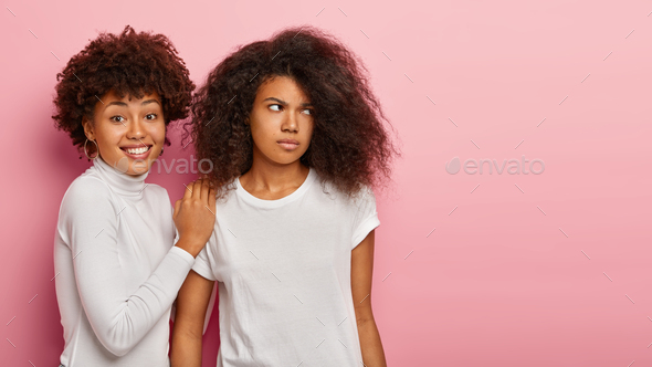 Shot of happy Afro woman supports her sister who has displeased sad face expression, focuses gaze as