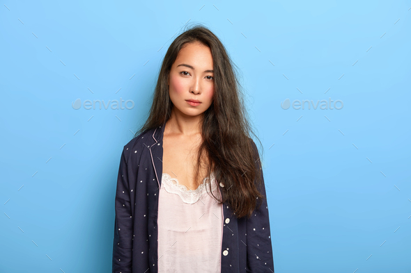 Photo of serious dissatisfied brunette Asian woman looks with tiredness at camera, has not enough sl